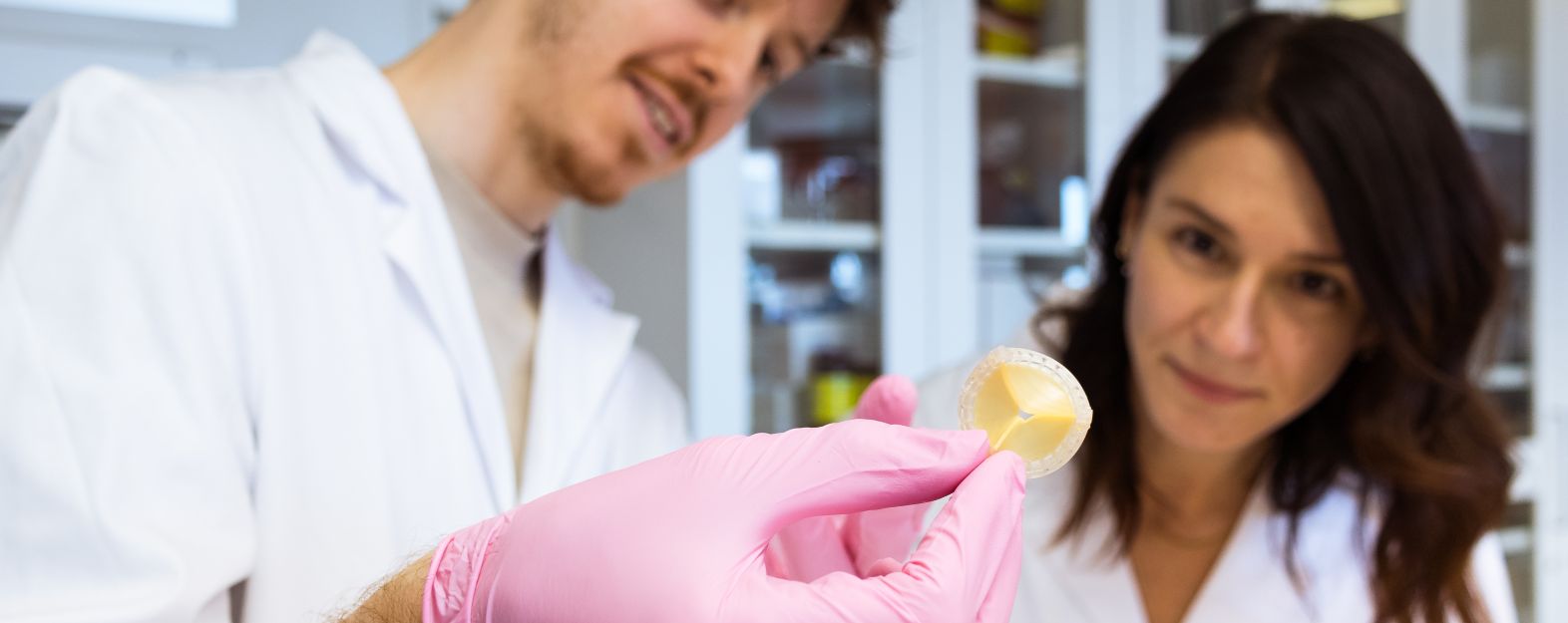 One male and one femal research in white alb coats looking at an artificial heart valve.
