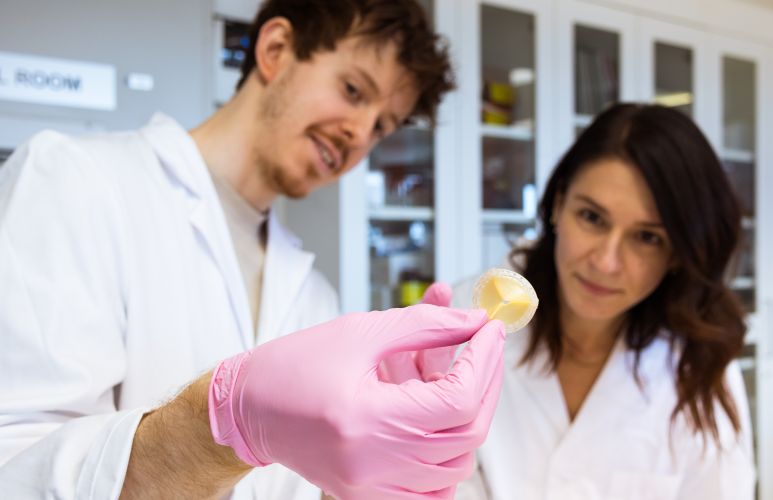 One male and one femal research in white alb coats looking at an artificial heart valve.
