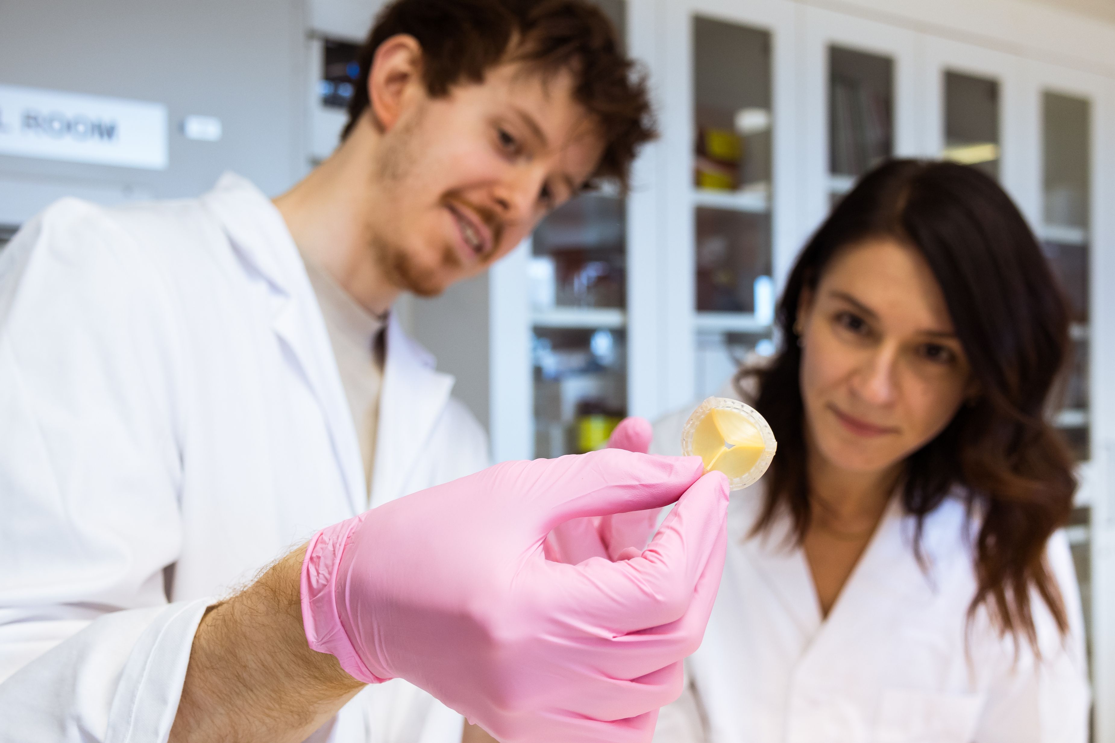 One male and one femal research in white alb coats looking at an artificial heart valve.