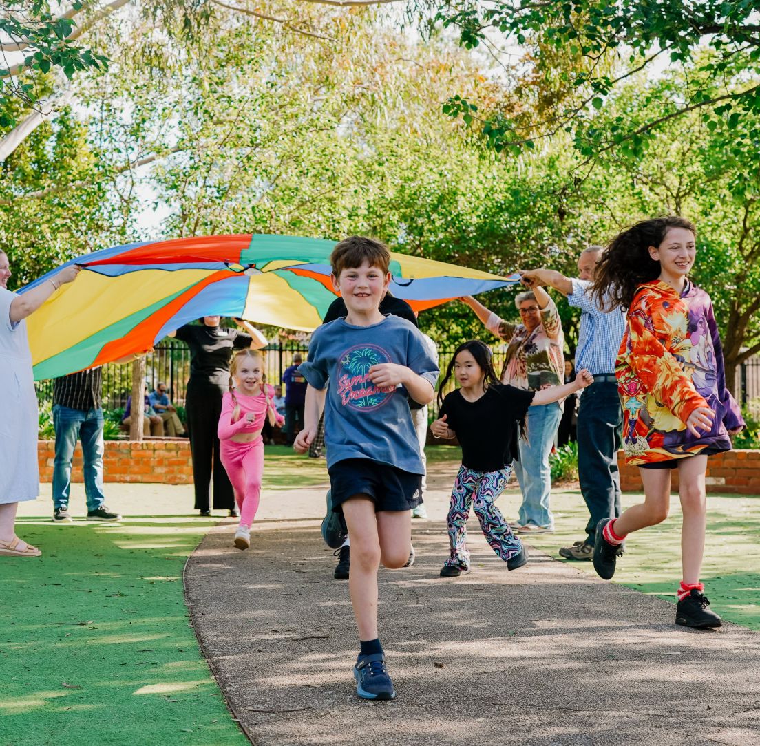 Children runing under a parachute held by adults