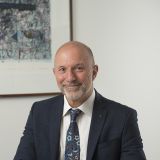 Middle-aged man wearing a sui tjacket and tie at a desk