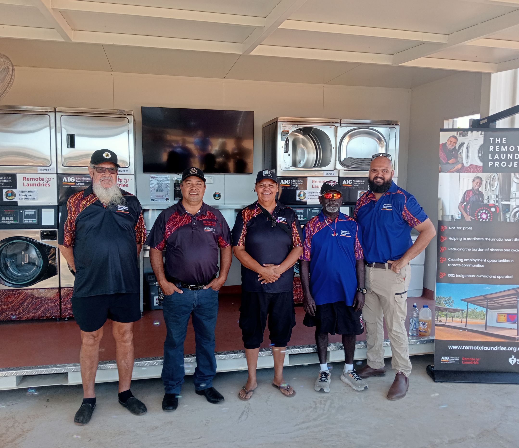 Five AIG board members standing in front of a remote laundry next to banner promoting the laundry