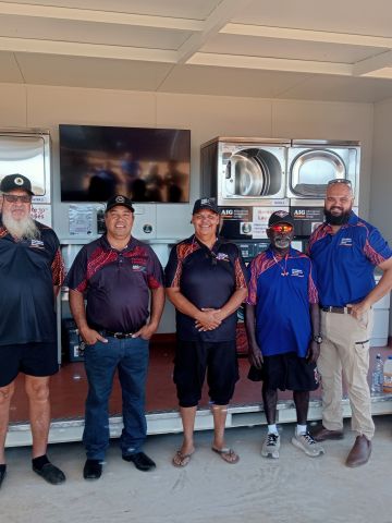 Five AIG board members standing in front of a remote laundry next to banner promoting the laundry