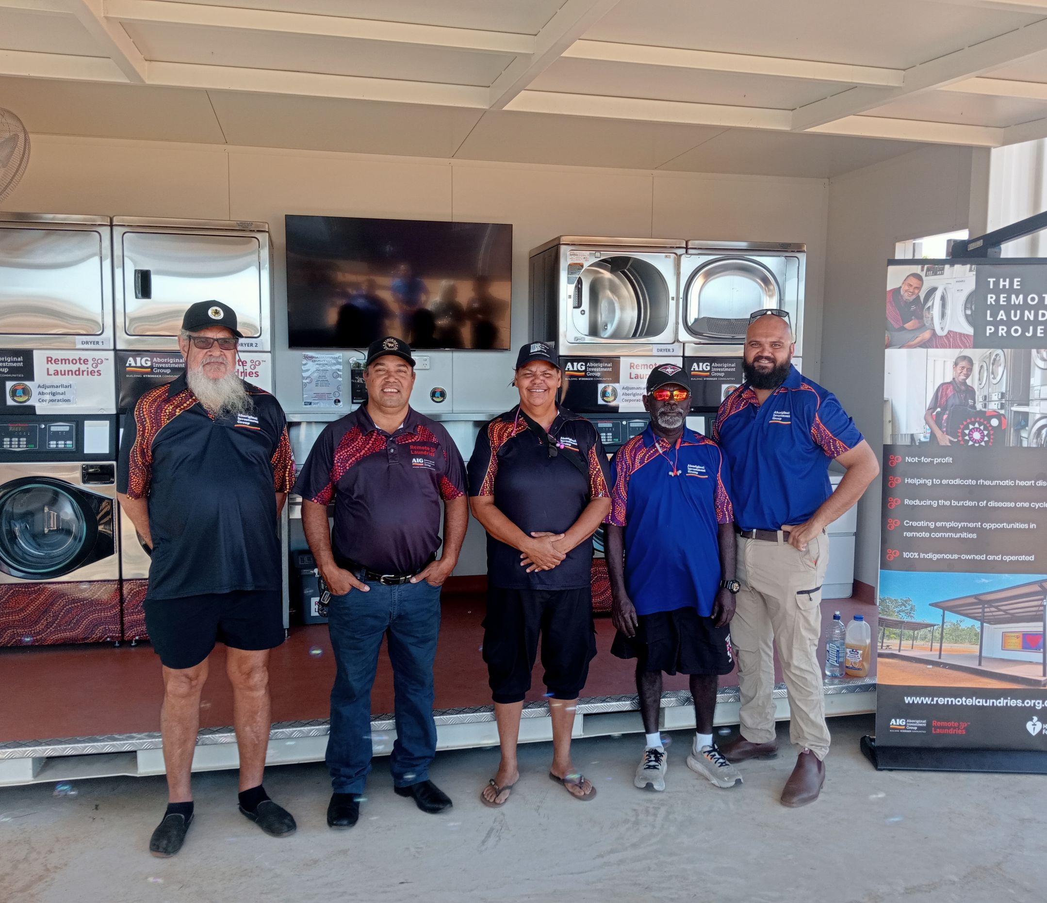 Five AIG board members standing in front of a remote laundry next to banner promoting the laundry