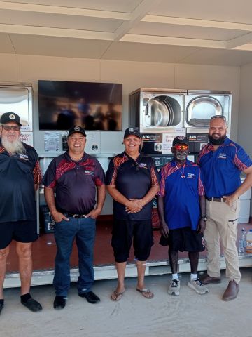 Five AIG board members standing in front of a remote laundry next to banner promoting the laundry