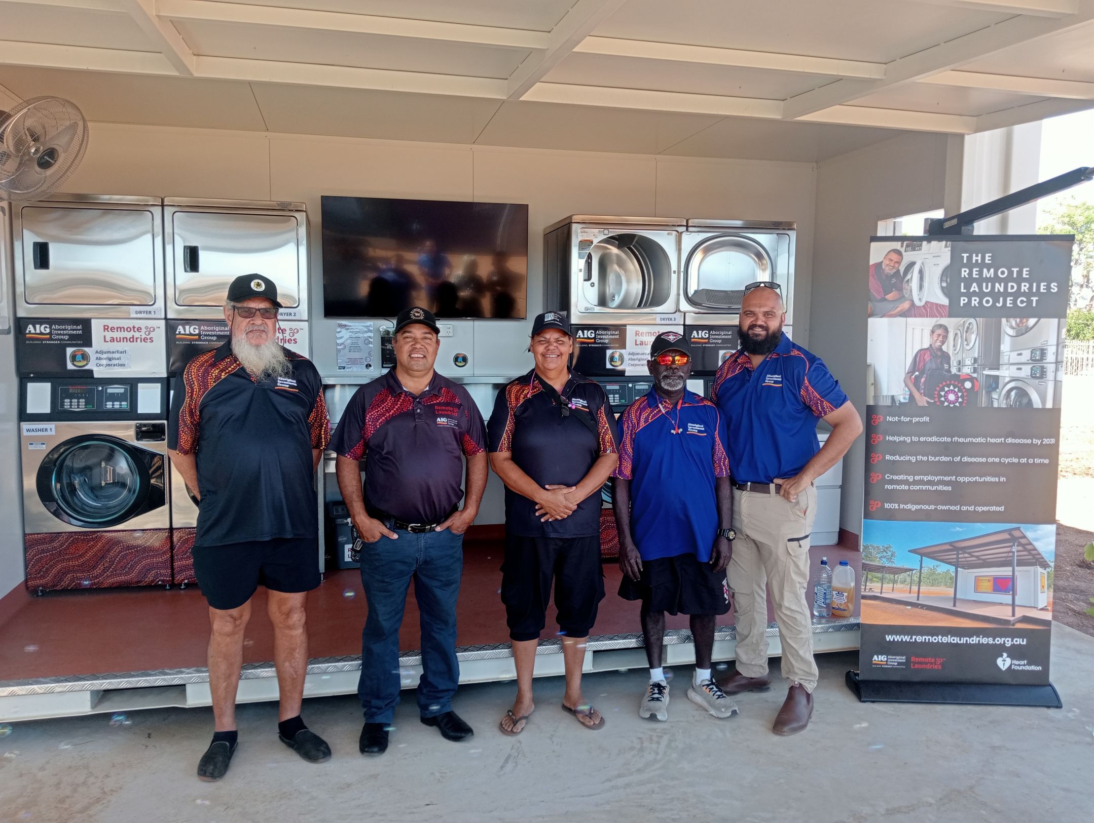 Five AIG board members standing in front of a remote laundry next to banner promoting the laundry