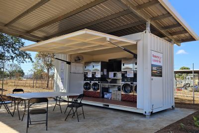Washing machines and dryers built into a freight container under a tin open shelter.