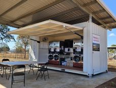 Washing machines and dryers built into a freight container under a tin open shelter.