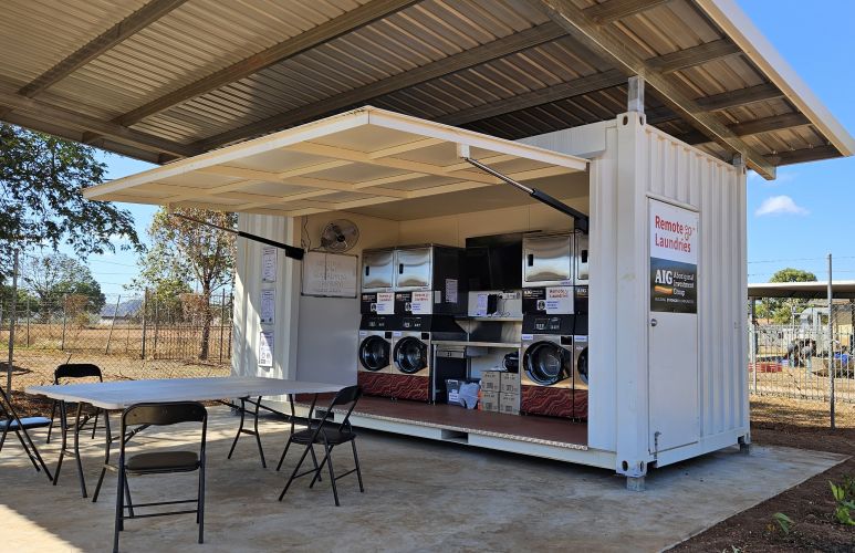 Washing machines and dryers built into a freight container under a tin open shelter.