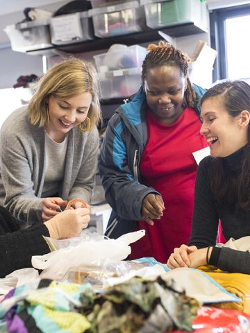 A group of 4 migrant women examining a handicraft seated and standign near table with fabric samples