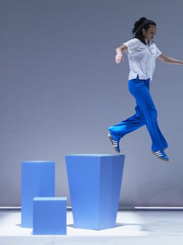 Young woman wearing a white top and blue pants captured mid air stepping off a blue plinth about a metre high