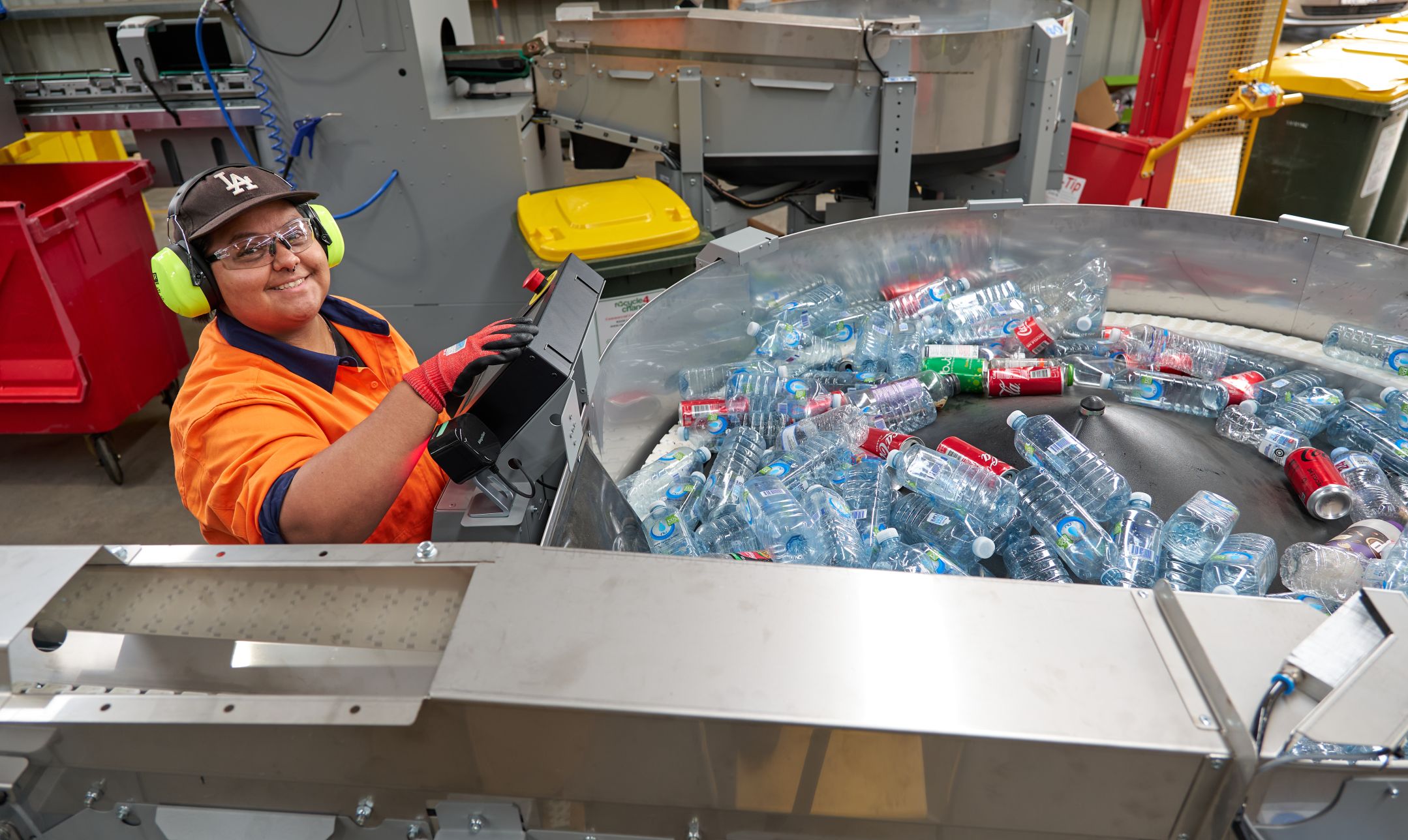 Woman in hi-vis and ear defenders at controls of a plsatic bottle sorting machine.
