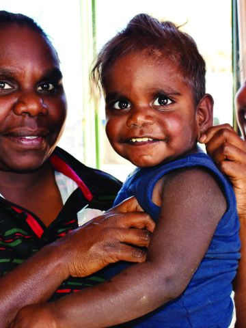 Two Aboriginal women cuddlding an Aboriginal toddler