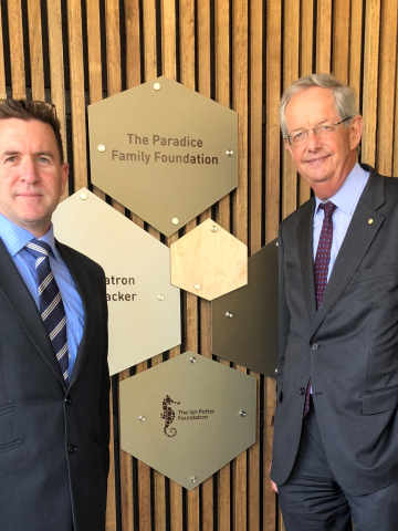 Two men in suits standing in front of signage acknowledging funders