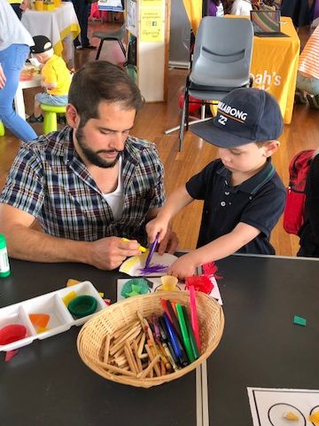 A man doing craft with his young son surround by other parents and pre-school age children
