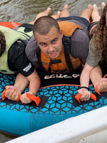 Three young people on a river raft hanging on the looking at the camera smiling.