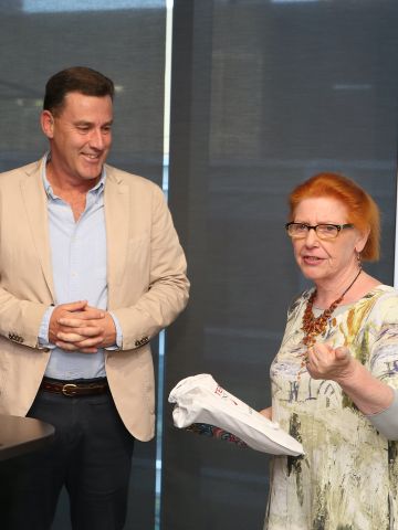 A middle-aged man standign looking at a middle aged woman who is speaking to an audience.