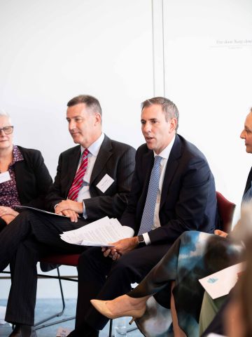 Two men in suits sitting in a larger group in a semi-circle
