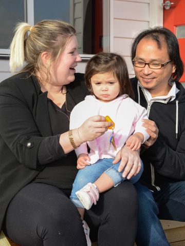 Two parents with young child in front of new house
