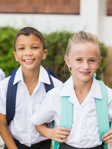 Three school aged children wearing uniforms and backpacks