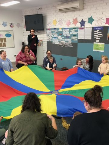 Parents and pre-school children holding a colourful parachute taut