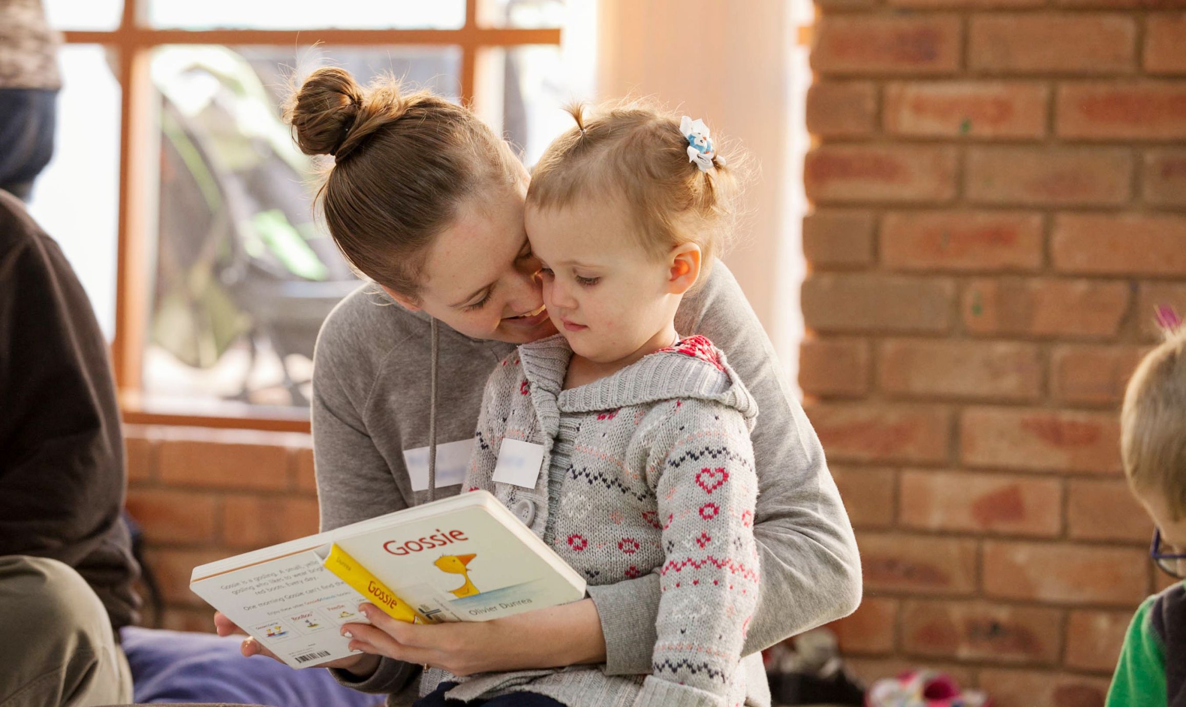 A mother with her arm aroudn her toddler reading a book