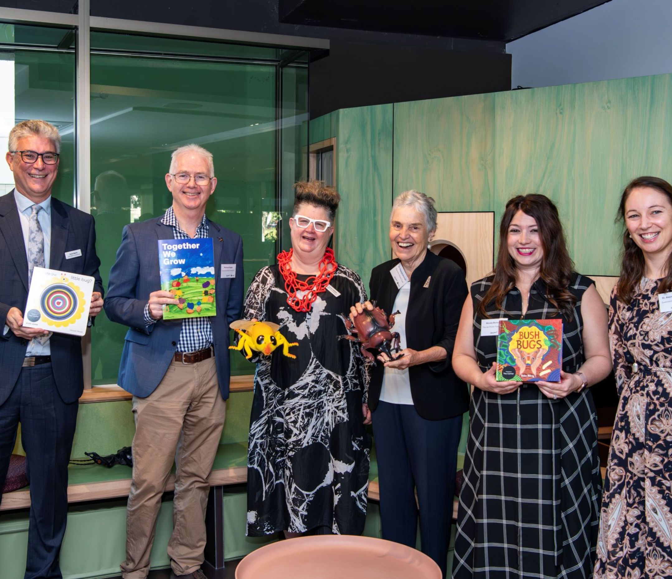 Two mena and four women holding children's books, smiling and looking to camera