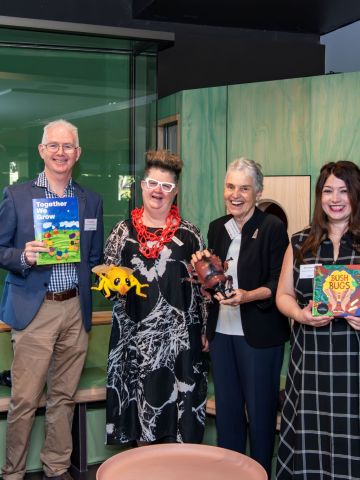 Two mena and four women holding children's books, smiling and looking to camera
