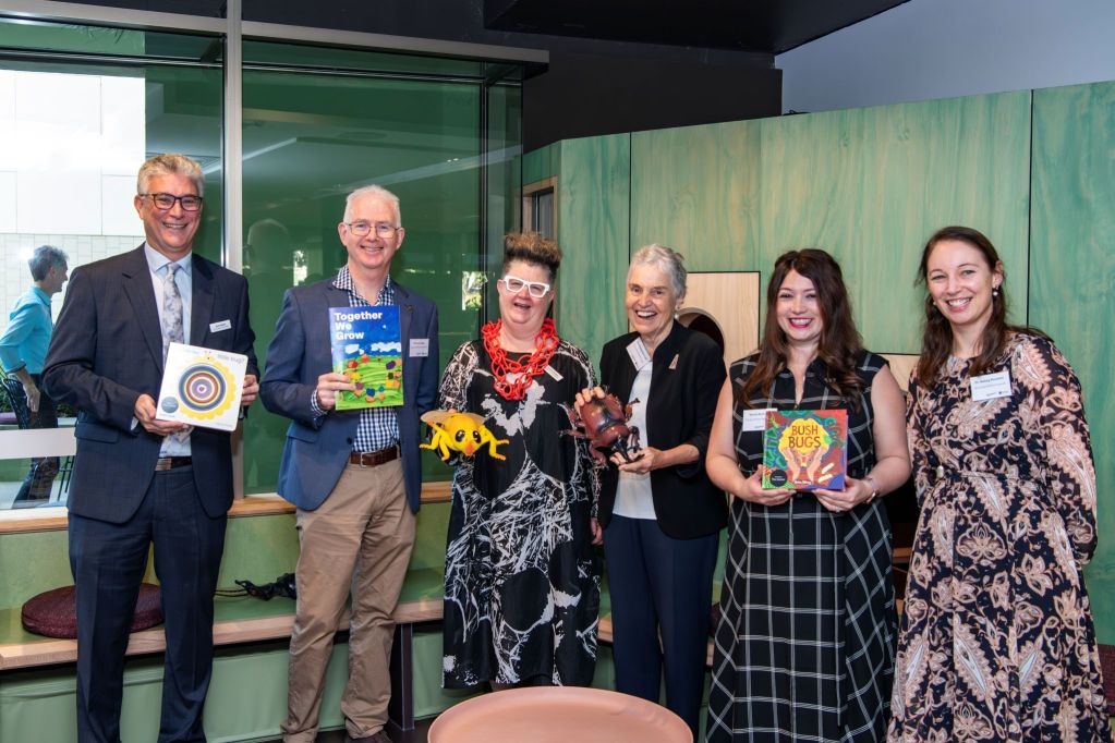 Two mena and four women holding children's books, smiling and looking to camera