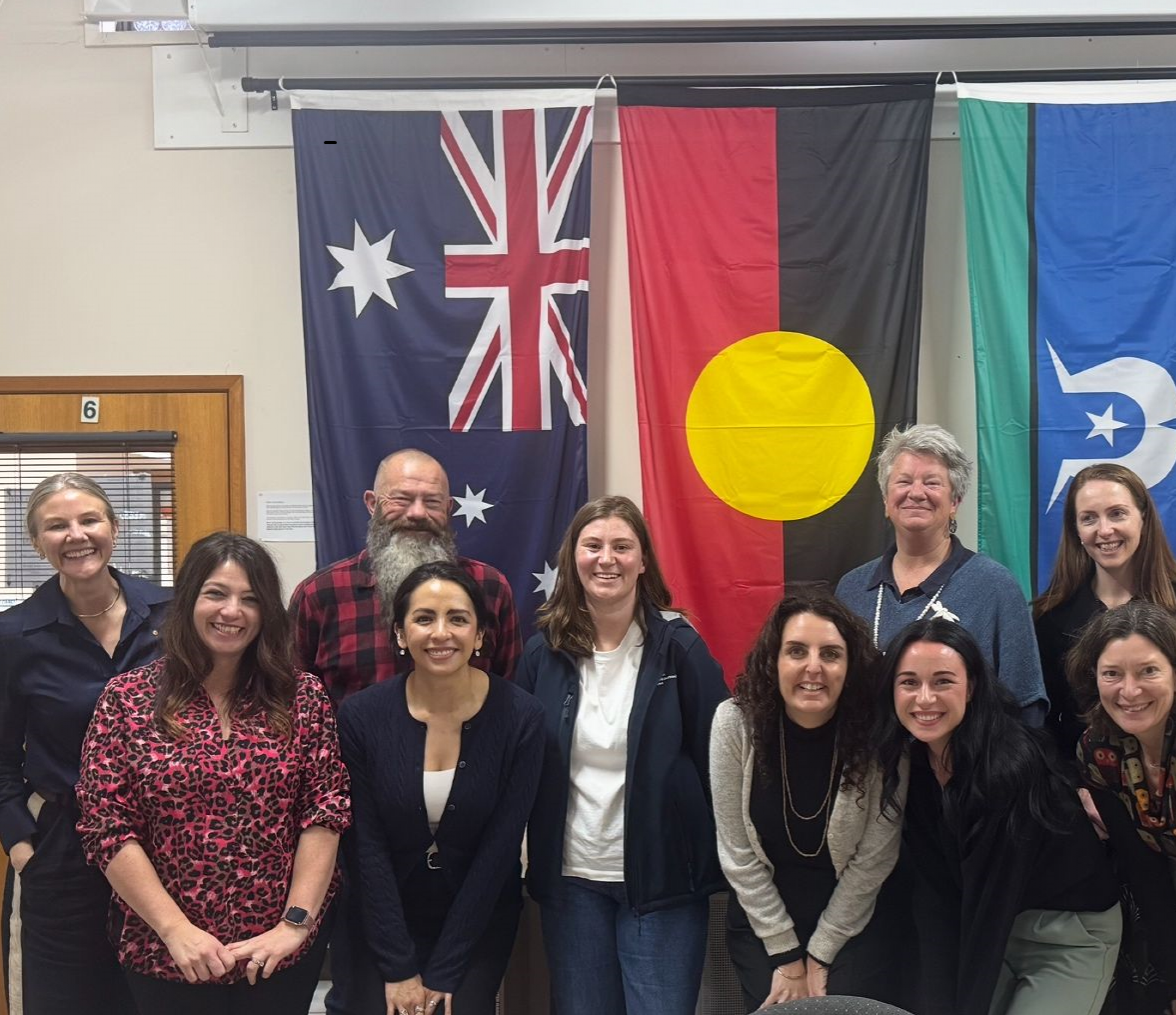 A group of 10 people smiling at the camera in front of the Australian, Aboriginal and Torres Strait Isalands flags.