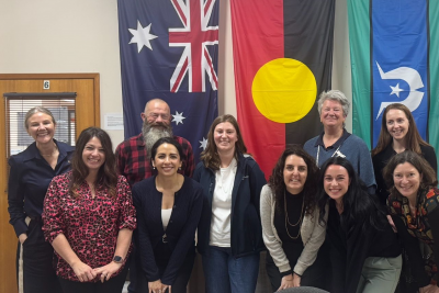 A group of 10 people smiling at the camera in front of the Australian, Aboriginal and Torres Strait Isalands flags.
