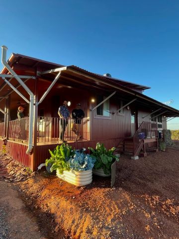 Two men standing on the verandah of a new house situated with red earth in the foregroudn and a blue sky in the background.