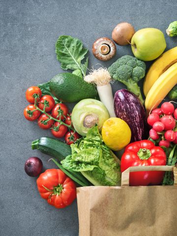 Fruit and vegetabkes spilling  out of a brown paper bag