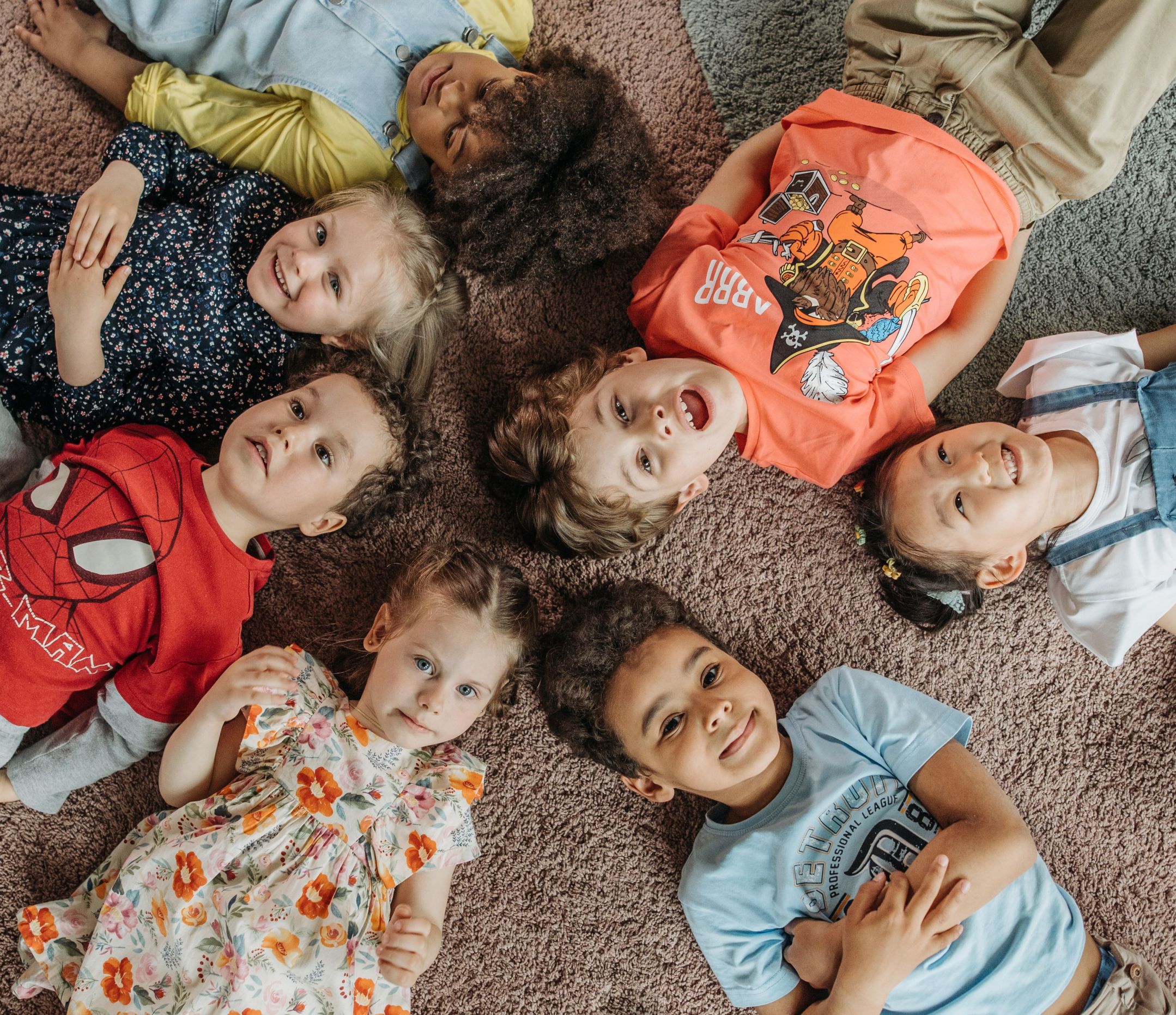 Aerial view of 7 pre-school aged children lying on their backs in a circle with their heads towards the middle.