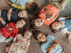 Aerial view of 7 pre-school aged children lying on their backs in a circle with their heads towards the middle.