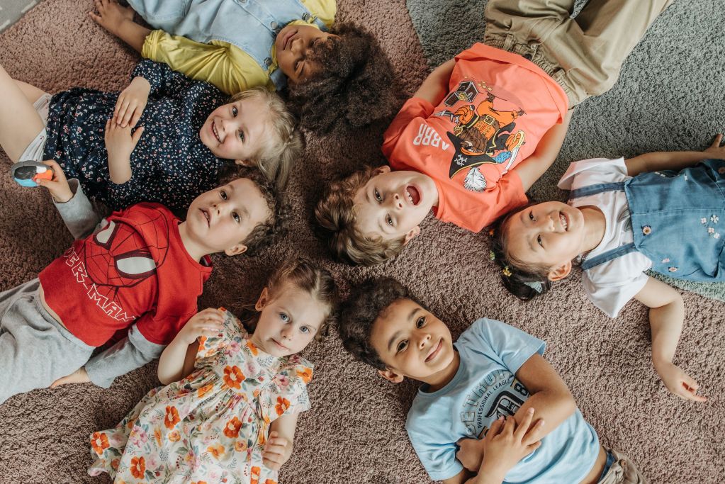 Aerial view of 7 pre-school aged children lying on their backs in a circle with their heads towards the middle.