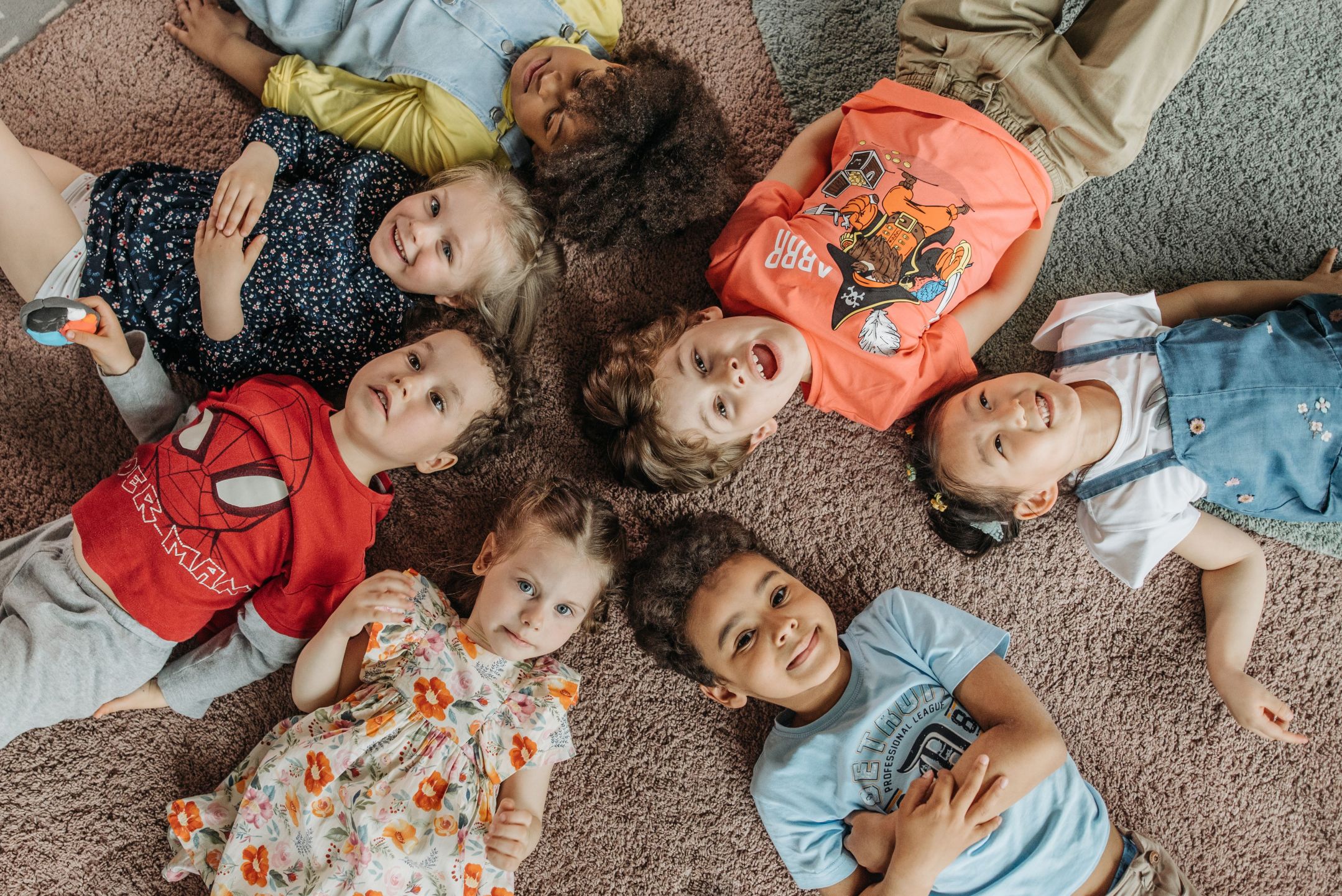 Aerial view of 7 pre-school aged children lying on their backs in a circle with their heads towards the middle.